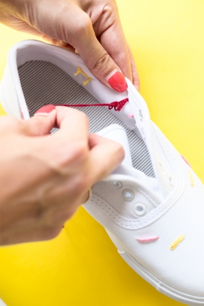 Someone sewing strings on a white sneaker 