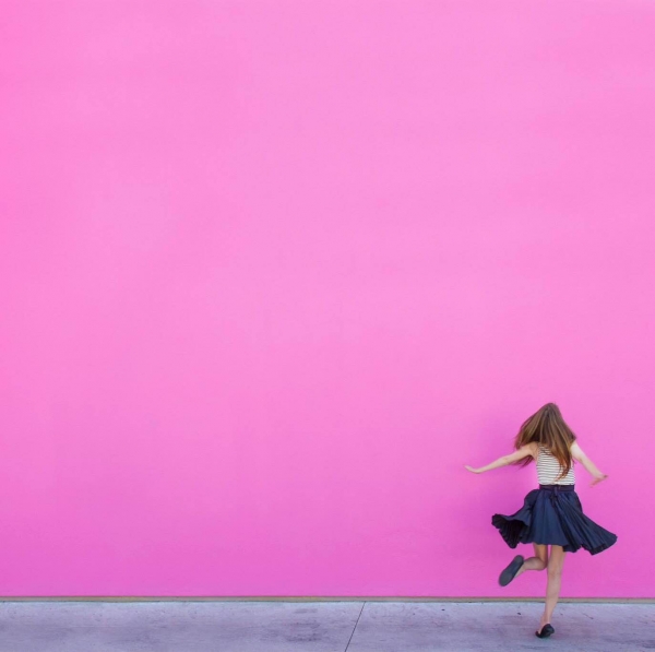 A woman walking in front of a pink wall