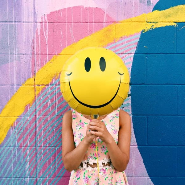 A woman holding a smiley face balloon