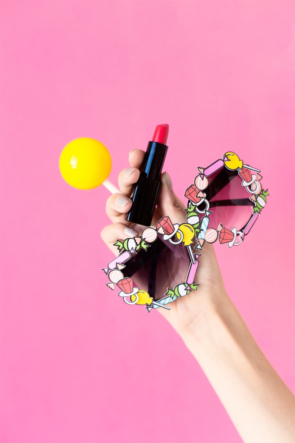 Someone holding glasses, lipstick, and a yellow ball