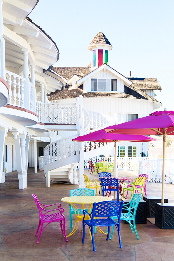 A white building with colorful chairs and tables outside of it