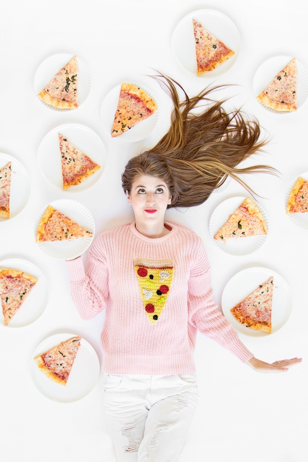 A woman wearing a pizza sweater, laying next to pizza