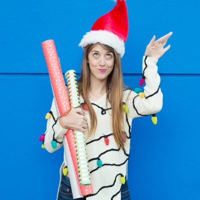 DIY Christmas Lights Sweater A woman wearing a santa hat and holding wrapping paper