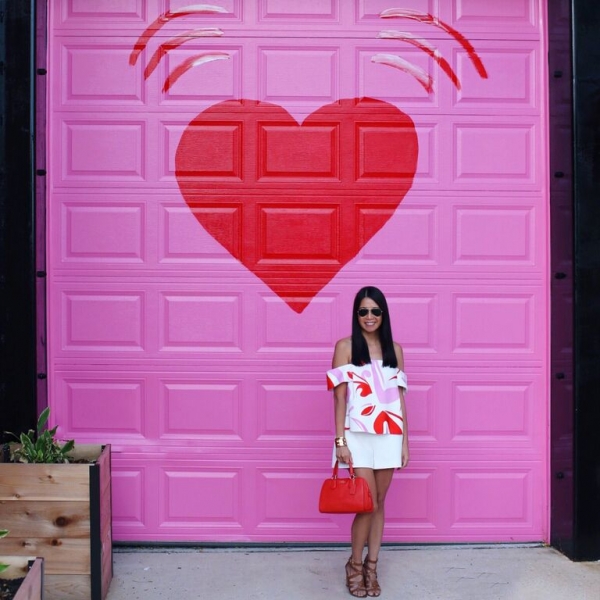 A woman with a white shirt and skirt in front of a pink garage