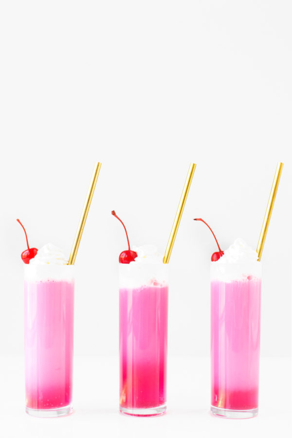 Three glasses with gold straws and pink liquid 