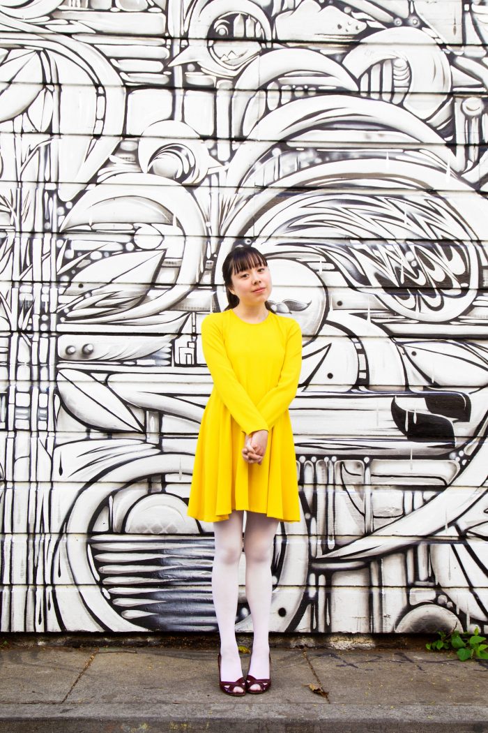 A woman in a yellow dress standing in front of a painted wall