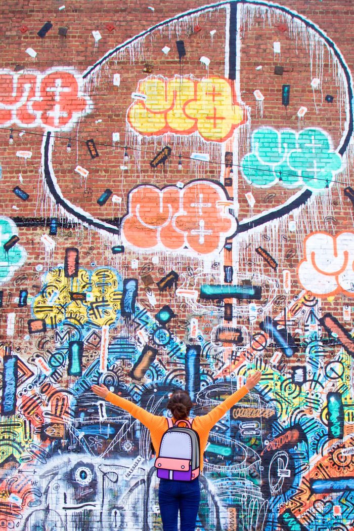 A woman standing in front of a graffiti brick wall