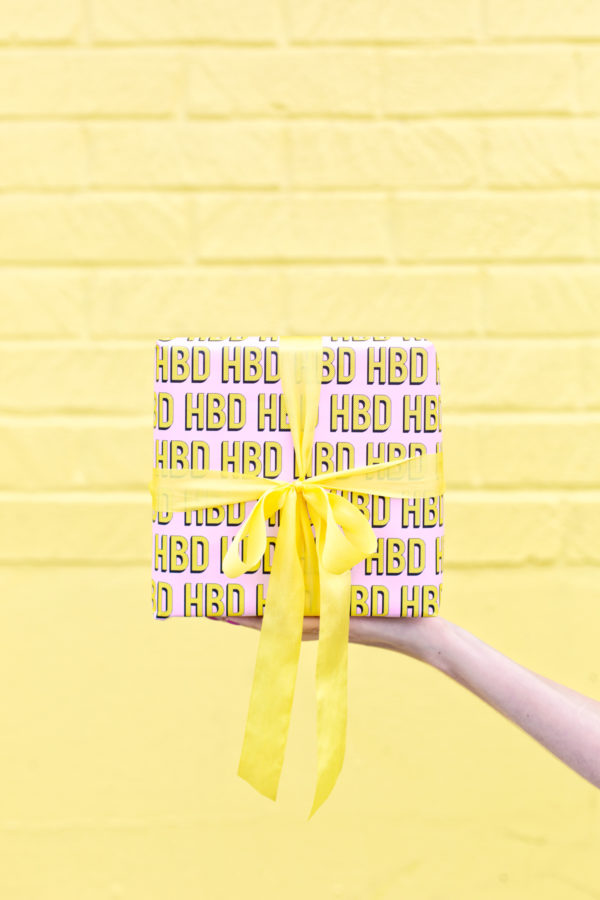 Someone holding a present in front of a yellow wall