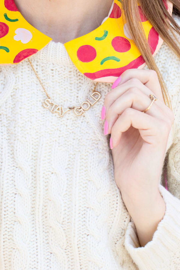 Someone wearing a necklace that says \"stay gold\"