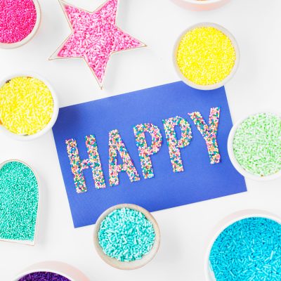 How To Dye Sprinkles! Containers with sprinkles and a paper that says "happy"