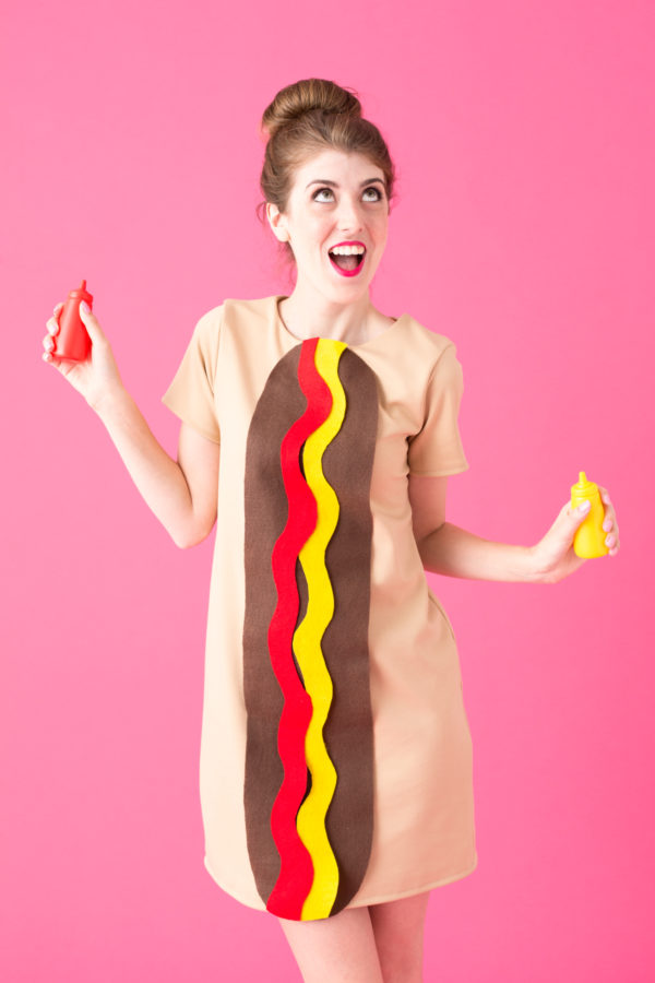 Hot Dog Halloween Costume A woman dressed up as a hot dog holding a bottle of ketchup and a bottle of mustard.