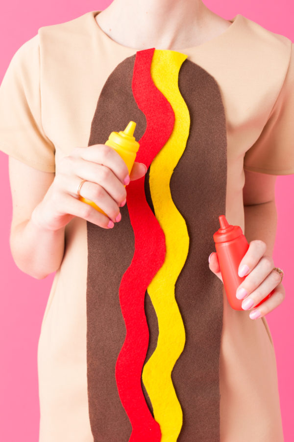 DIY Food Costumes A woman dressed as a hot dog and holding ketchup and mustard.