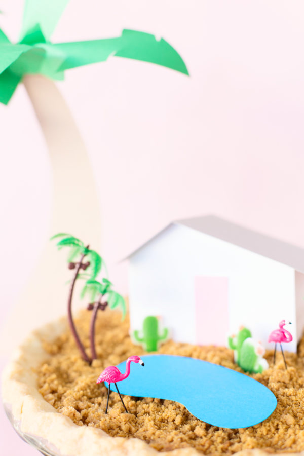 A pie with a house and fake palm trees on it