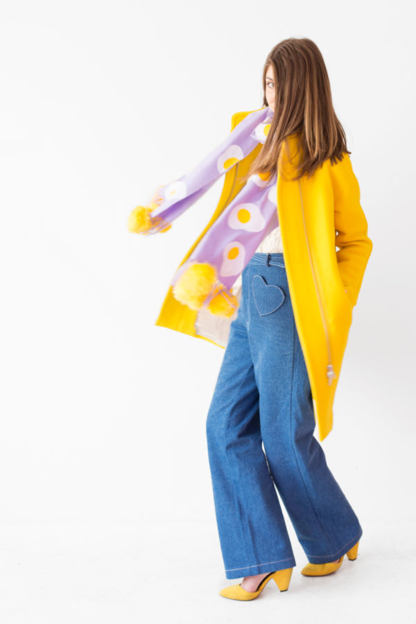 A woman wearing a purple scarf with eggs on it and a yellow jacket