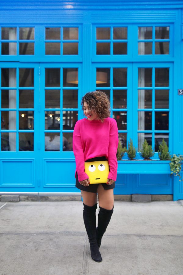 A woman standing in front of a building wearing a pink sweater