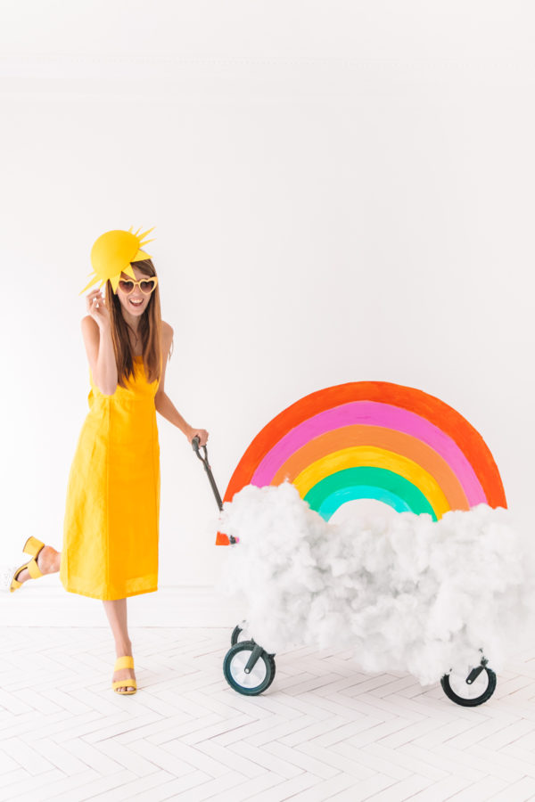 Someone dressed as a sun pushing a rainbow in a cart