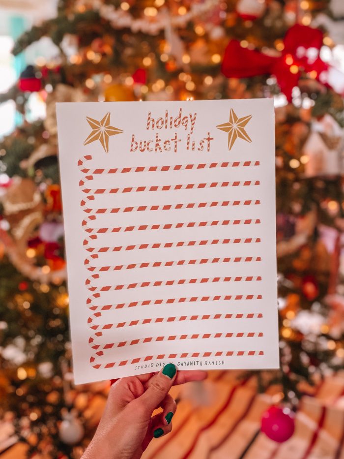 Holiday Bucket List PDF Hand holding a piece of paper with candy canes printed on it.