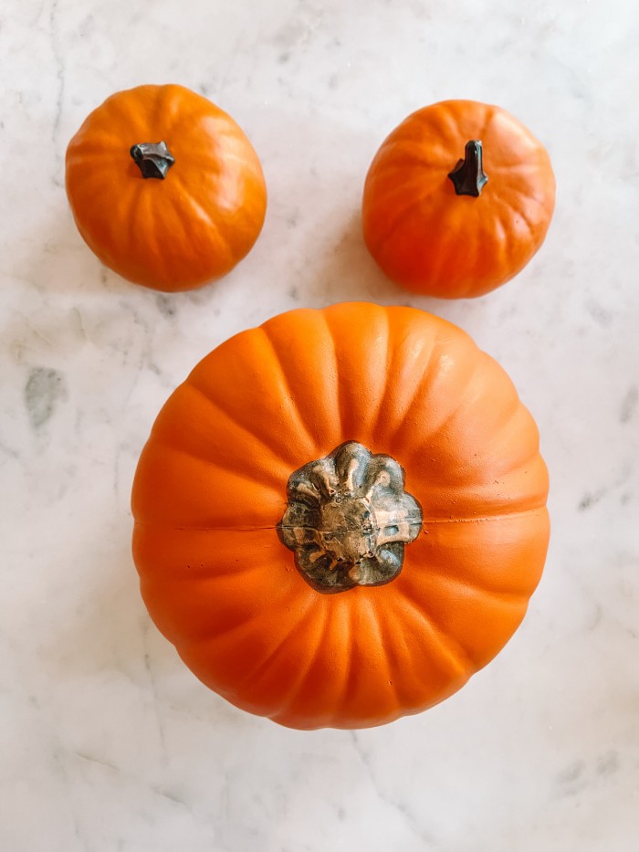 One large pumpkin with two small pumpkins above it on marble table