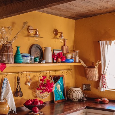 A Bold, Layered & Moody Yellow Kitchen yellow kitchen with wood ceiling and shelf with colorful decor and dishes