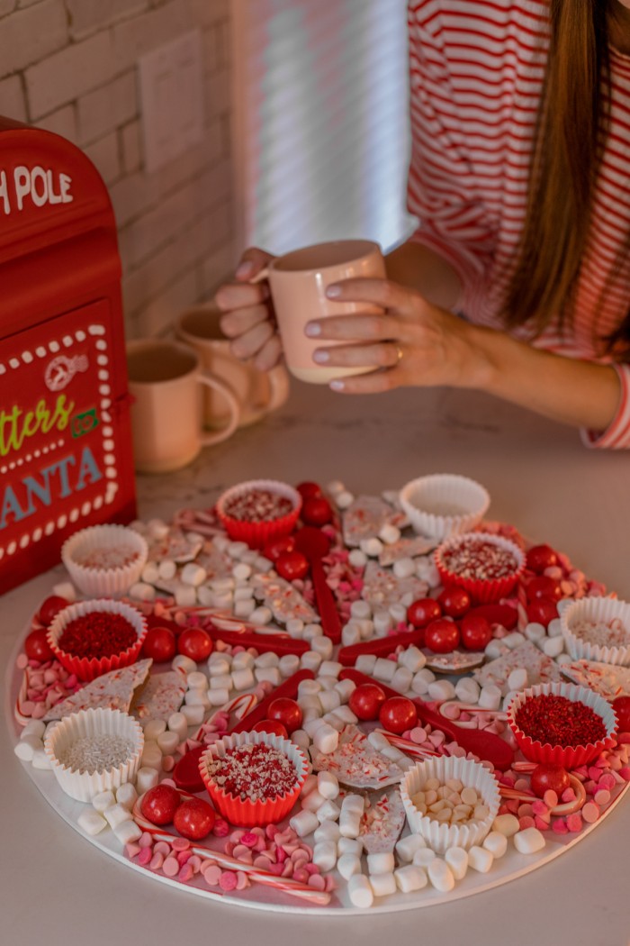 Easy Hot Chocolate Board Christmas hot chocolate board with woman in background holding a pink mug.