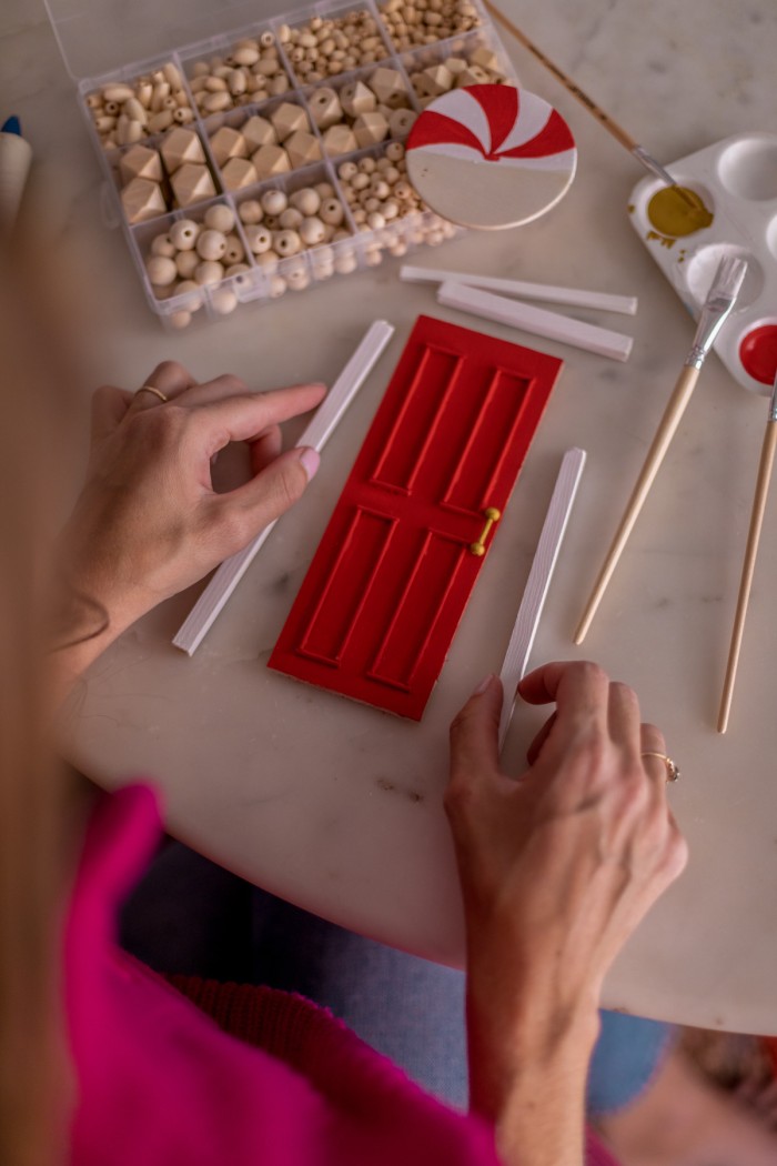 Hands holding two wooden dowels to create a frame around the small red door. 