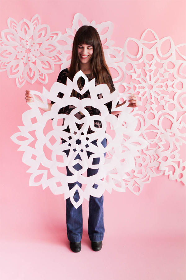 Snowflake Christmas Costume Woman holding a large paper snowflake with more snowflakes on the pink wall behind her.