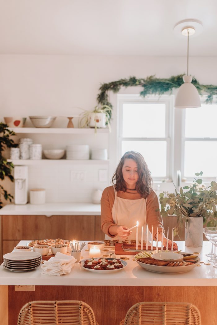Woman lighting a candle with appetizers on the table next to her. 