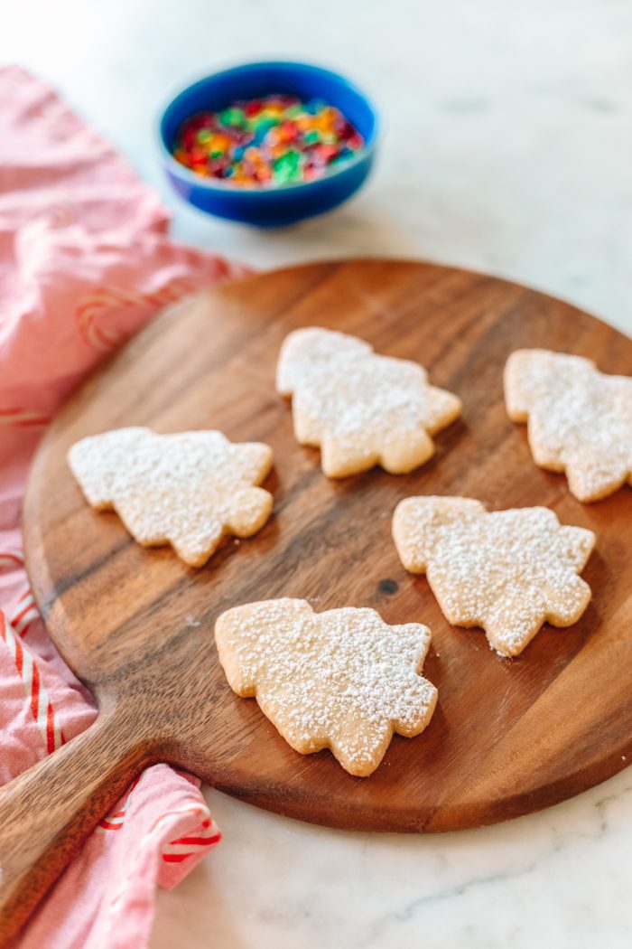 Ideas for a Holiday Bucket List Sugar cookies in the shape of trees on a wooden cutting board.