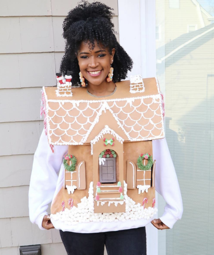 Gingerbread House Costume Woman standing in front of a house while wearing a cardboard gingerbread house.