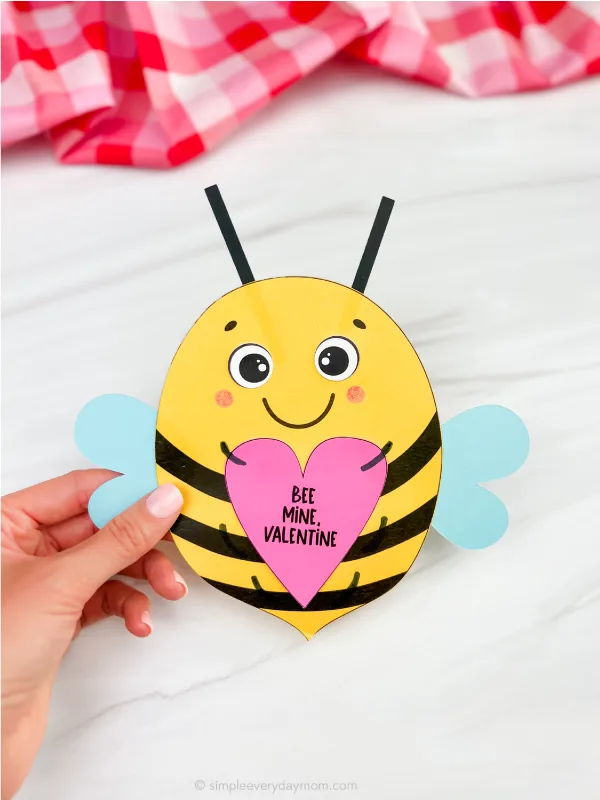 Bee Valentine Hand holding a valentine shaped like a bee out of paper.