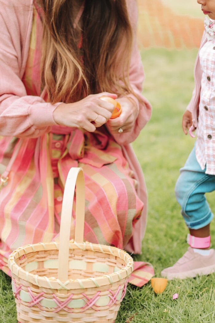 Easter Hunt Woman opening a plastic egg while kneeling in front of a woven easter basket.