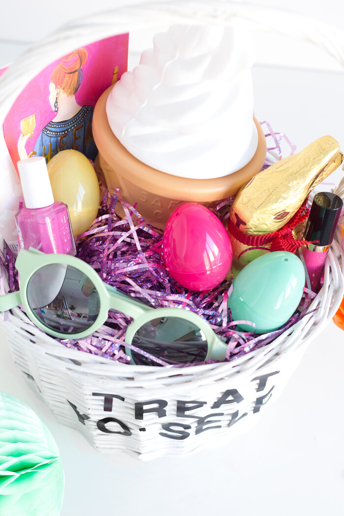 Creative Easter Basket White basket filled with purple shredded paper with sunglasses, nail polish, lipstick and chocolate in the basket.