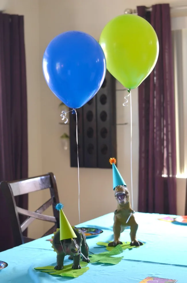 Dinosaur Party Two dinosaur figures on a table with party hats and balloons.