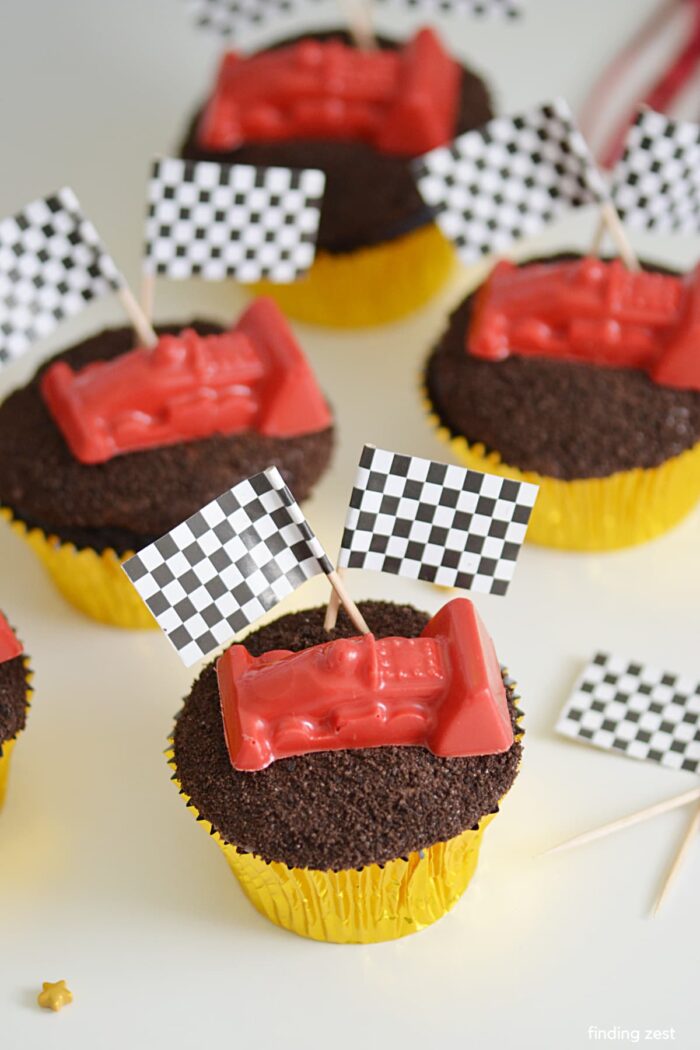 Race Car Party Cupcakes topped with crushed cookies and a race car with flags.