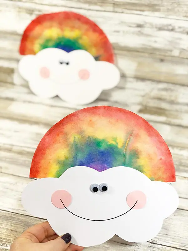Hand holding a paper cloud with a coffee filter rainbow on top of it. 