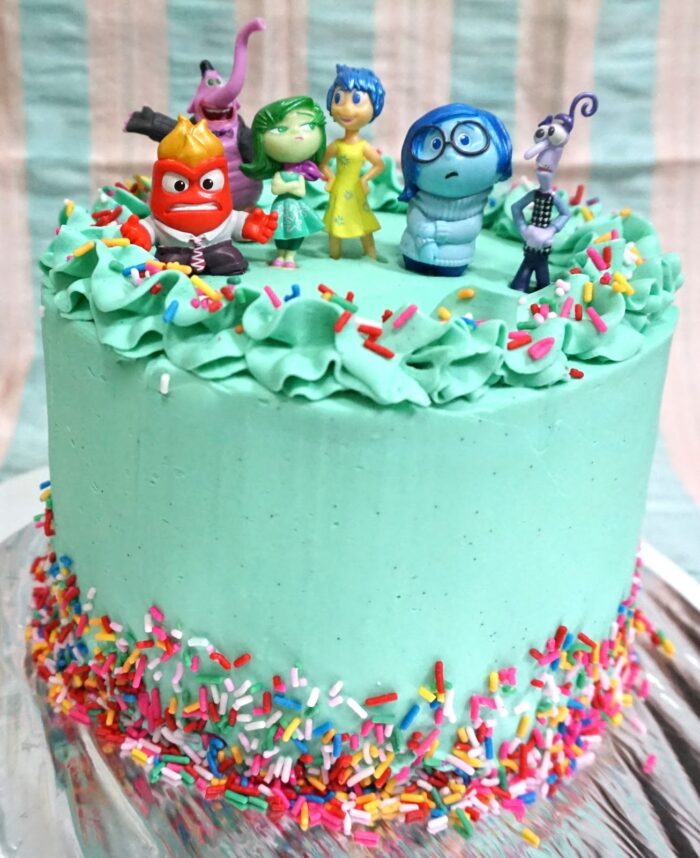 Inside Out Rainbow Cake Blue cake with rainbow sprinkles and Inside Out character figures on top.