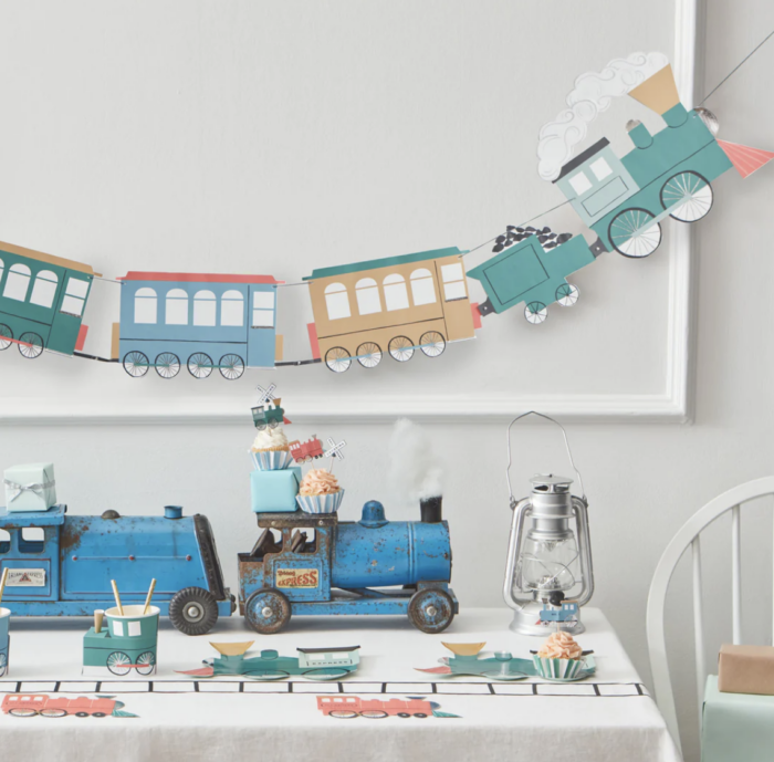 All Aboard Birthday Party Train garland hanging on the wall with a table with train decorations on it.