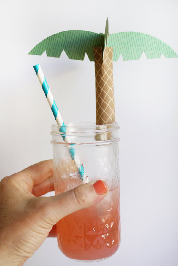 Drink Palms Hand holding a glass that is topped with a paper palm topper.
