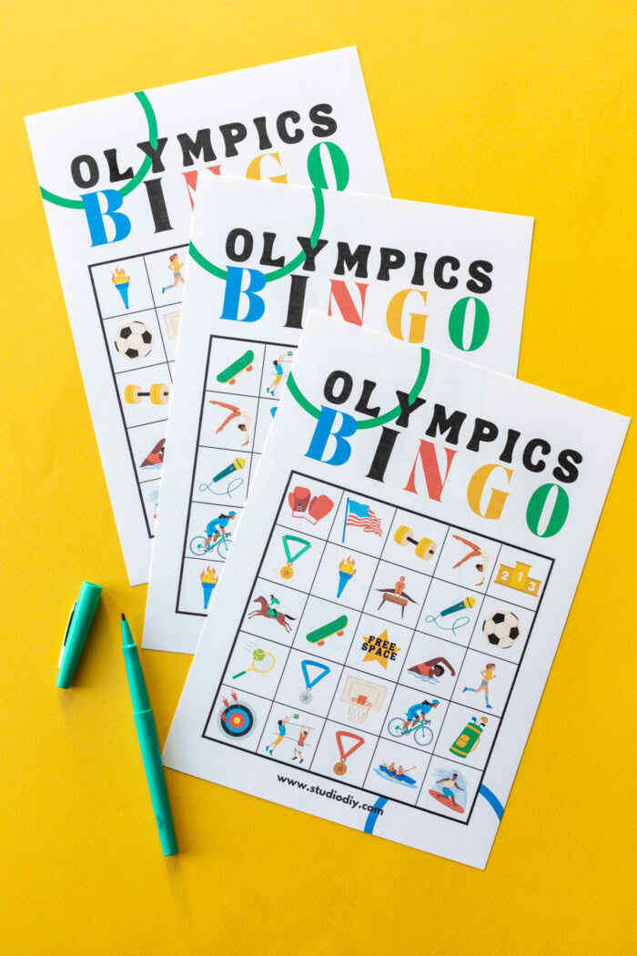 Summer Olympics Bingo Three Olympics bingo cards on a yellow background next to green markers.