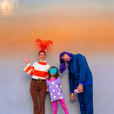 DIY Inside Out 2 Costumes Family wearing Inside Out 2 costumes in front of ombre wall